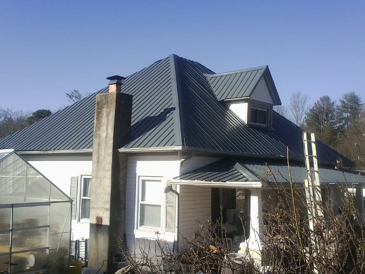 Dark blue standing seam metal roof on a white farmhouse with dormer — Slate & Tile Roof Repair by Roofing Brothers in Lahoma