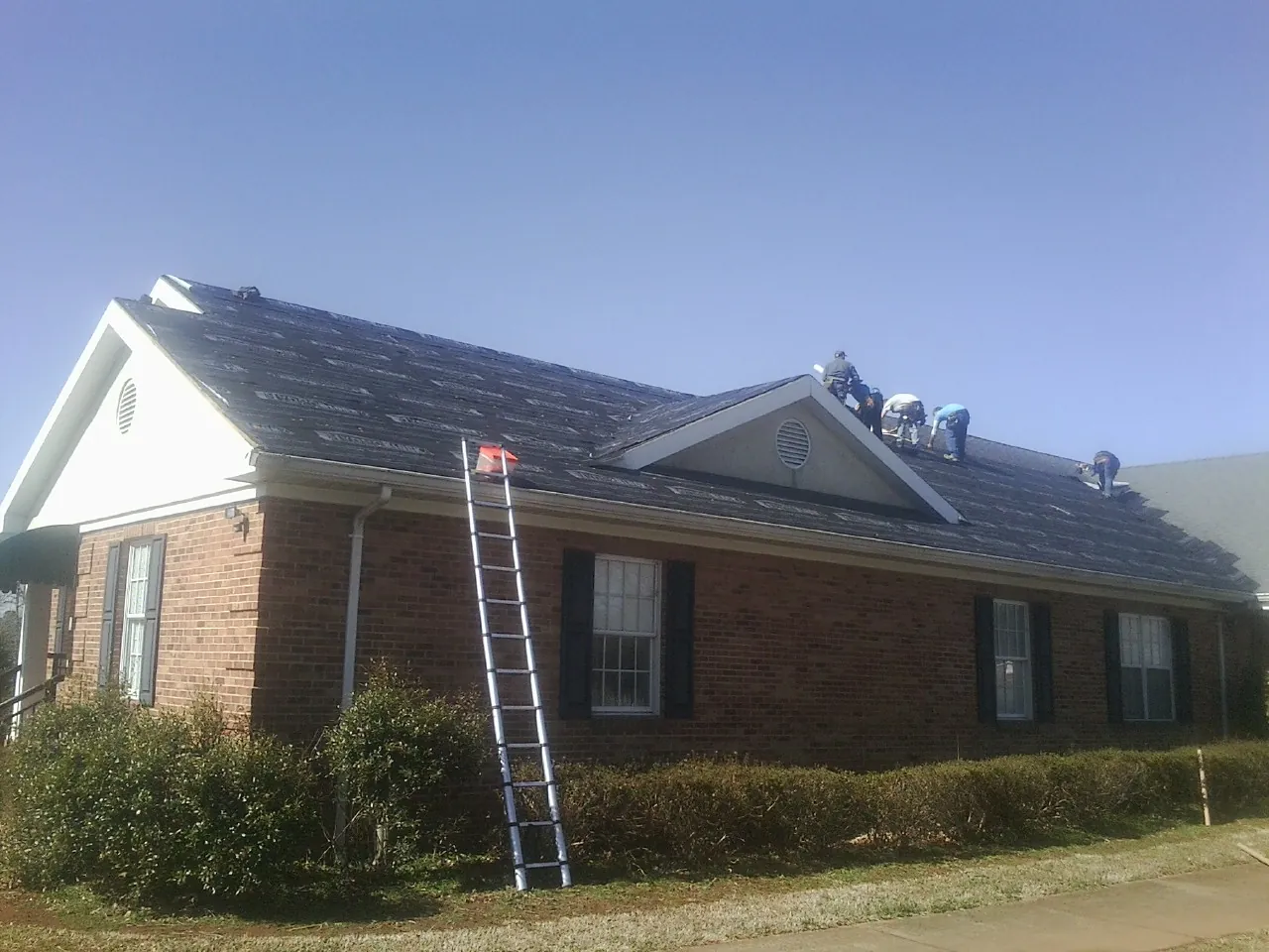 Crew tearing shingles off a brick ranch roof with a ladder set — Emergency Roof Repair work by our crew in Lahoma