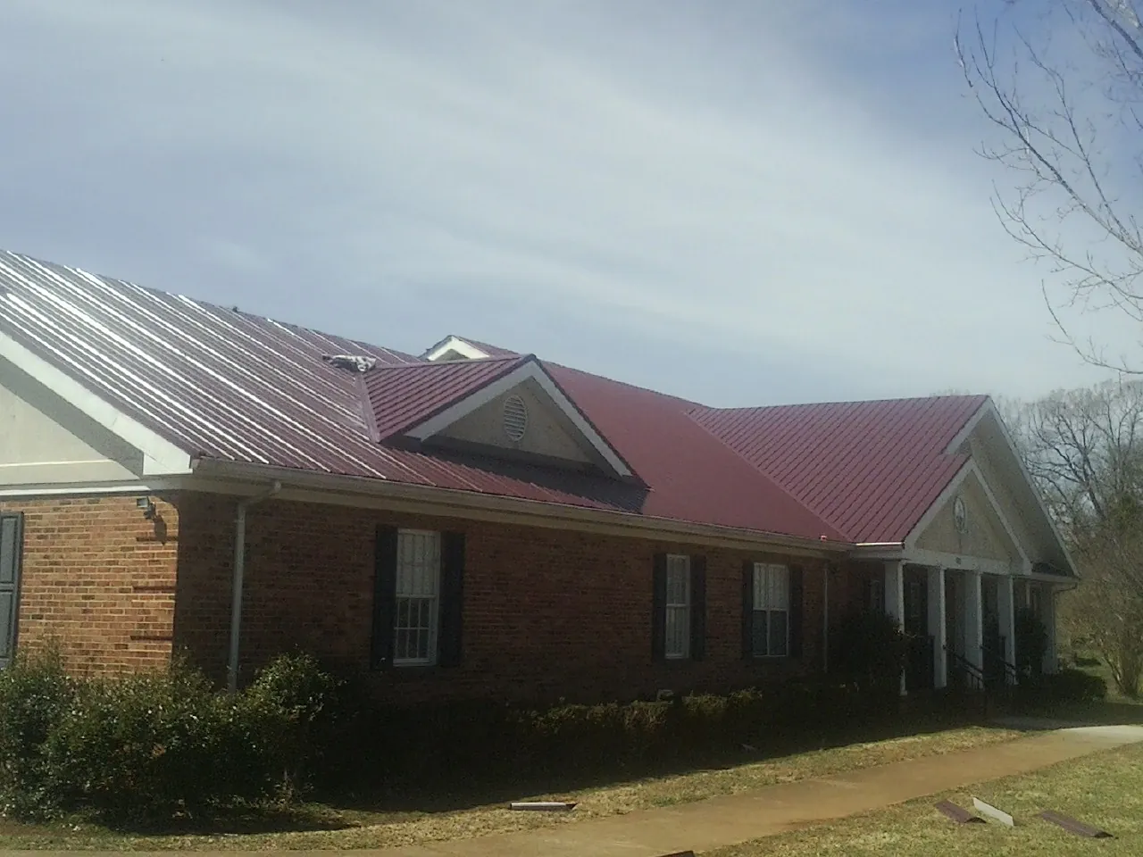 Red metal roof with gabled entries on a long brick building, from a Hail Damage Roof Repair job in Lahoma