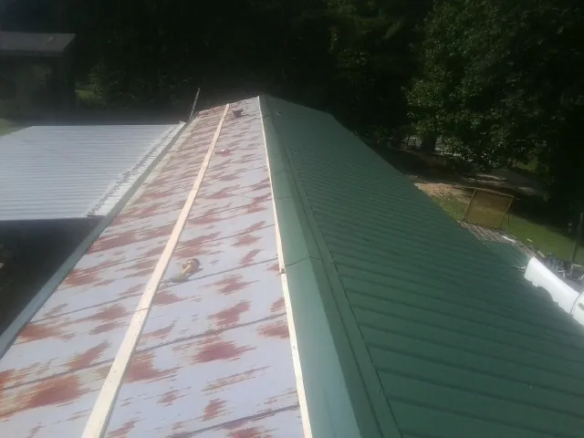 Old rusted panels beside newly installed green metal roofing — Wind Damage Roof Repair by Roofing Brothers in Lahoma