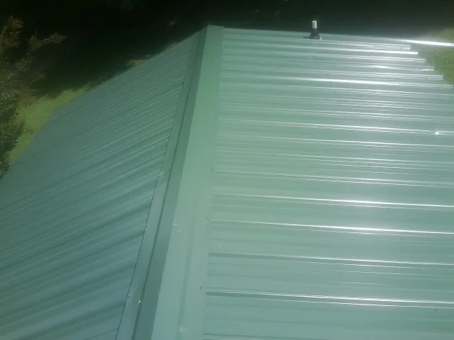 New green metal panels meeting at the ridge of a roof — Flat Roof Repair work by our crew in Lahoma
