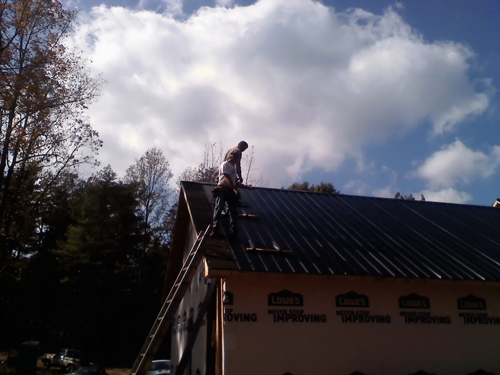 Roofer fastening dark metal panels high against a cloudy sky, from a Roof Inspection job in Lahoma
