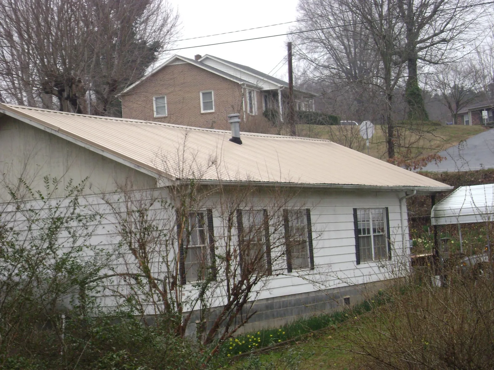 Tan metal roof on a white sided house set into a hillside — Commercial Roofing by Roofing Brothers in Lahoma