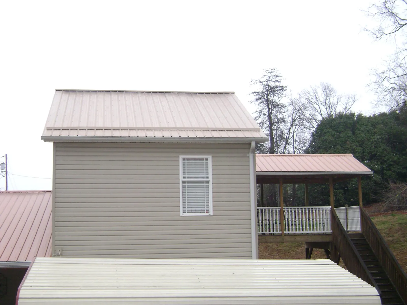 Tan metal roofs on a two story addition and attached porch, from a Roof Replacement job in Lahoma